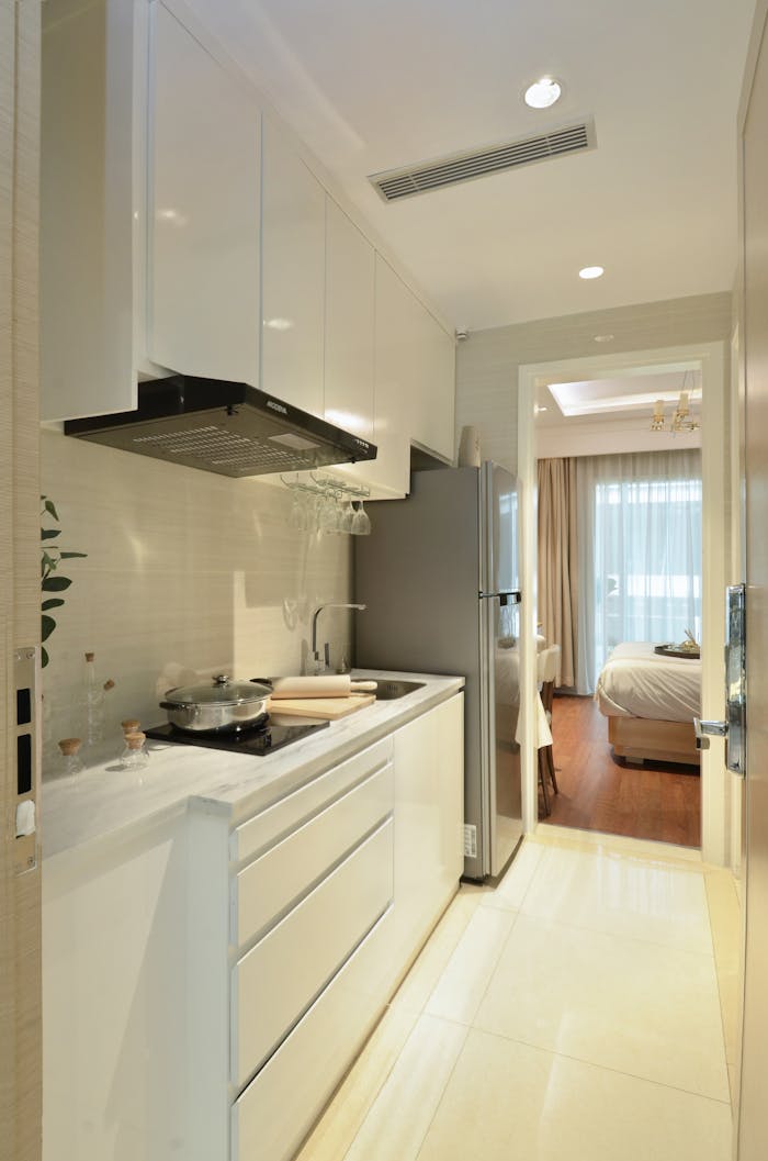 about-03 Modern white kitchen with sleek cabinets and stainless steel appliances, leading to a bright living area.